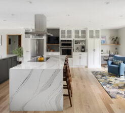 A view of the central kitchen island and seating area in the New Brighton Upgrade remodel. The white marble, waterfall countertop on the island shows the grey veining in the stone.
