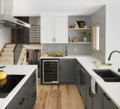 One side of the center island in the New Brighton Upgrade kitchen renovation with the stove, and across from it the kitchen sink and wine fridge. White upper cabinets with dark grey lowers. White marble countertops.
