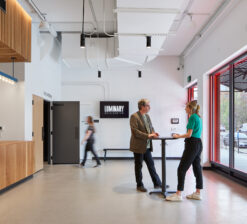 The main lobby of the Luminary Arts Center in Minneapolis, MN with two people standing at a circular high top table inside with another person walking behind them into the theater entrance. The concession/ticket stand can be seen on the left.