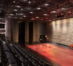 The main theater space, including the seating, main staircase, red performance floor, and historic limestone wall backdrop in the Luminary Arts Center performance space in Minneapolis, MN.