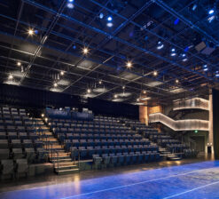 The theater seating, illuminated main staircase, and tension wire lighting grid suspended from the ceiling in the Luminary Arts Center performance space in Minneapolis, MN.