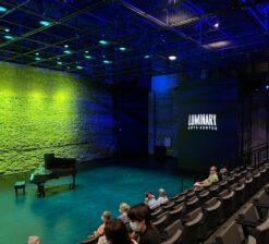 The main theater space, including the seating, performance floor, and historic limestone wall backdrop with a grand piano in the center at the Luminary Arts Center performance space in Minneapolis, MN.