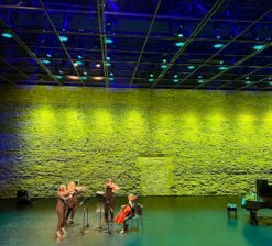 The main theater space and historic limestone wall backdrop with a quartet of string instruments playing live at the Luminary Arts Center in Minneapolis, MN.