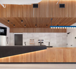 The concession and ticket booth at the Luminary Arts Center in Minneapolis, MN. A charcoal concrete waterfall bar top is accented by a white oak slatted soffit overhead (which is also wrapped on the exterior of the island) and a blue light fixture reminiscent of a classic theater marquee sign.