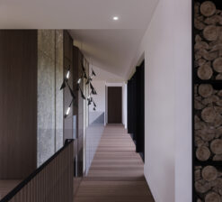 An interior rendering of the entry corridor with a floor-to-ceiling glass wall overlooking the courtyard on the right, and a floor-to-ceiling stone wall to the left in the Sirkel Kjøre residence. Tall storage for fireplace wood is visible on the edge of the hallway.