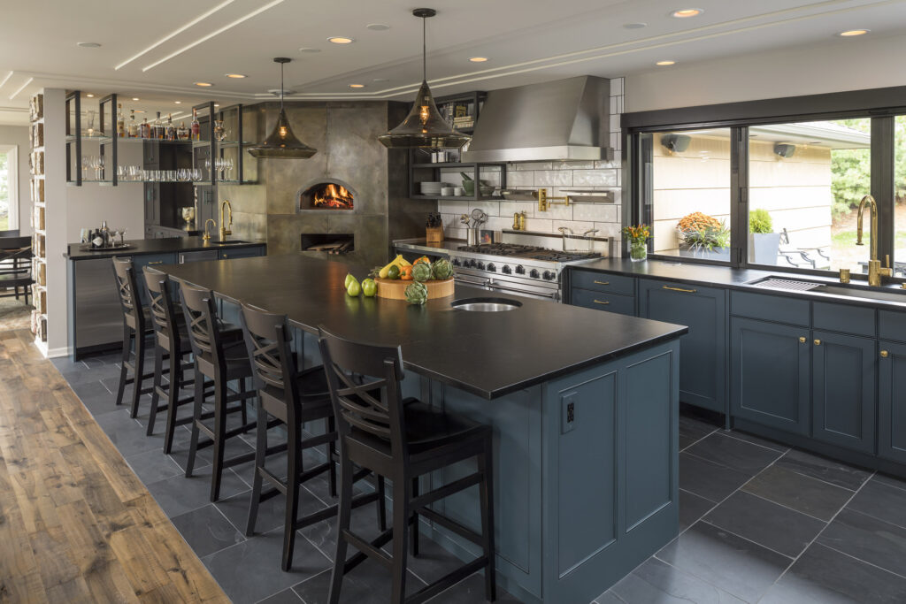 The Culinary Workshop kitchen showing the large central island with barstools, a pizza oven, and large accordion window to the backyard.