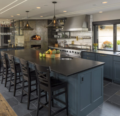 The Culinary Workshop kitchen showing the large central island with barstools, a pizza oven, and large accordion window to the backyard.