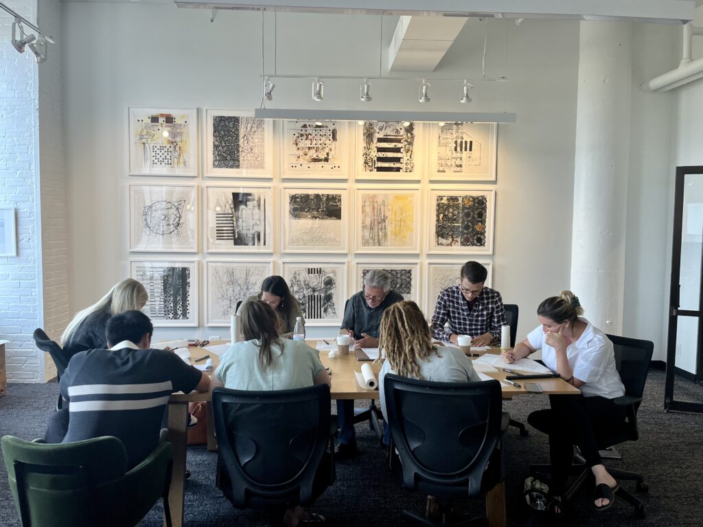 The Shelter Architecture and Interior Design team seated around a large table sketching during a design brainstorm.