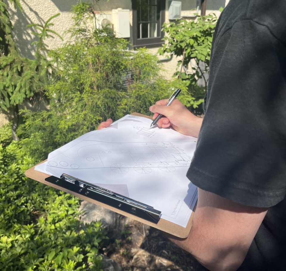A Shelter Architecture and Interior Design team member drawings measurements by hand onto a printed plan during a site documentation visit.
