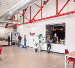 An interior view of the HUGE Improv entry vestibule, box office desk, concessions, and theater entrance with pops of red accents throughout in the chairs and overhead supports.