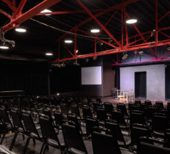 A side view of the HUGE Improv Theater and the audience seating and stage for live performances with red arches overhead.