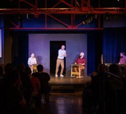 Four male actors on stage at the HUGE Improv Theater performing a live show.