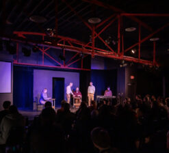 Four male actors and one female actress on stage at the HUGE Improv Theater during a live show. The audience is seated and watching the show.