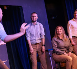 Three male actors and one female actor on stage during a live performance at the HUGE Improv Theater.